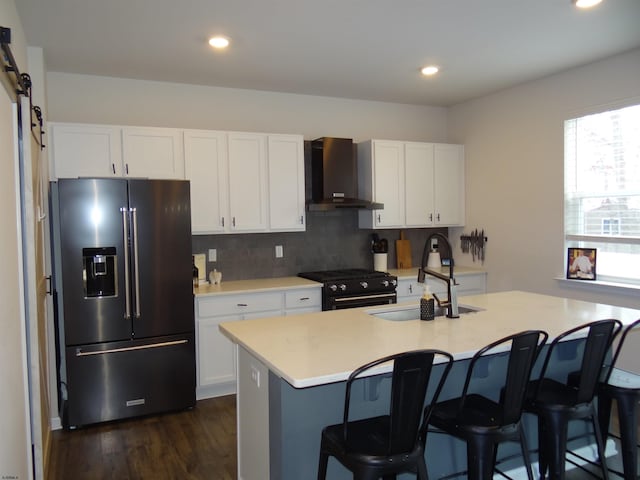 kitchen featuring a barn door, a sink, high end fridge, wall chimney range hood, and gas stove