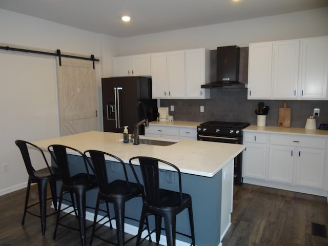 kitchen featuring a barn door, white cabinets, a sink, black appliances, and wall chimney exhaust hood