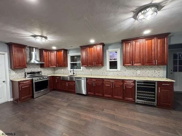 kitchen featuring wine cooler, dark wood finished floors, stainless steel appliances, wall chimney exhaust hood, and a sink