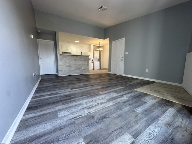 unfurnished living room with an inviting chandelier, baseboards, visible vents, and dark wood-type flooring