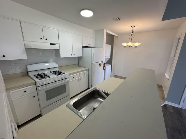 kitchen with white appliances, tasteful backsplash, stacked washer and dryer, under cabinet range hood, and a sink