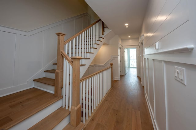 stairway with recessed lighting, a decorative wall, and wood finished floors