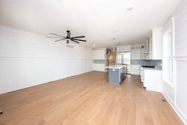 kitchen featuring light wood finished floors, white range with gas cooktop, a center island with sink, light countertops, and backsplash