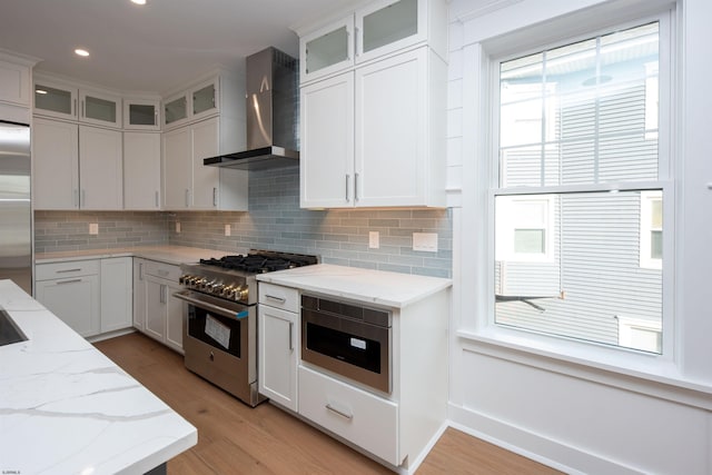 kitchen featuring light wood-type flooring, wall chimney exhaust hood, appliances with stainless steel finishes, and tasteful backsplash