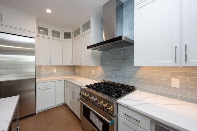 kitchen with wall chimney exhaust hood, white cabinetry, high end appliances, and backsplash