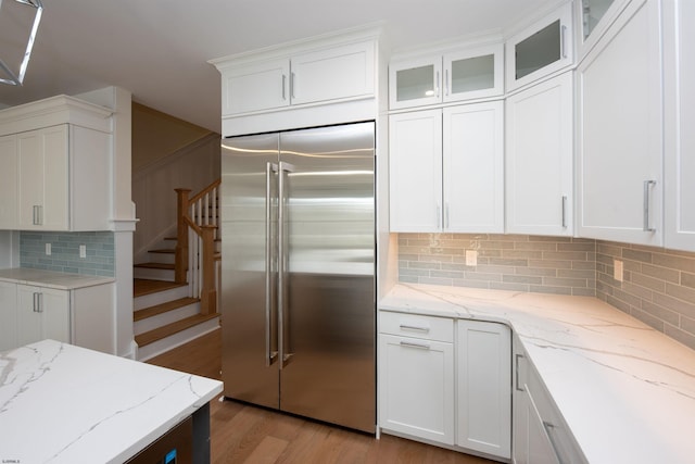 kitchen featuring light wood finished floors, stainless steel built in refrigerator, decorative backsplash, and white cabinets