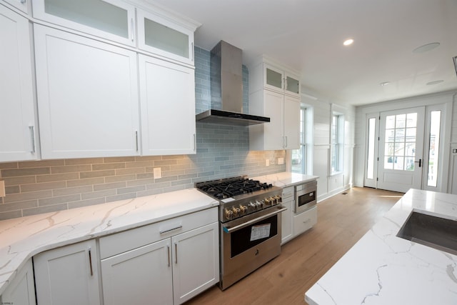 kitchen featuring white cabinets, wall chimney exhaust hood, built in microwave, stainless steel stove, and light wood-style floors