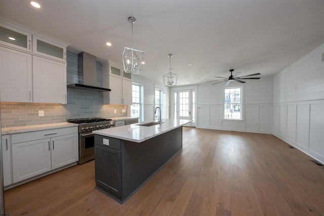 kitchen featuring a kitchen island with sink, a sink, wall chimney range hood, wood finished floors, and high end stove