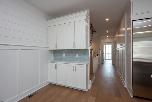 kitchen featuring light wood finished floors, tasteful backsplash, visible vents, light countertops, and built in fridge