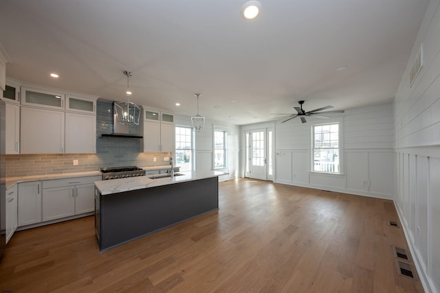 kitchen with decorative backsplash, stove, a sink, wall chimney range hood, and light wood-type flooring