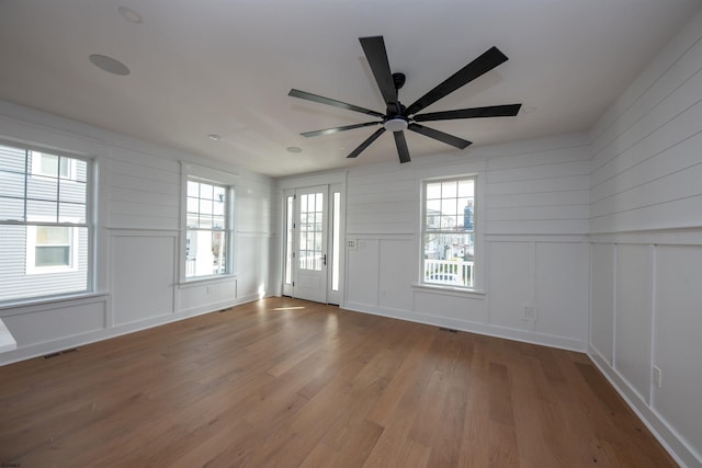 interior space with a ceiling fan, wood finished floors, visible vents, and a decorative wall