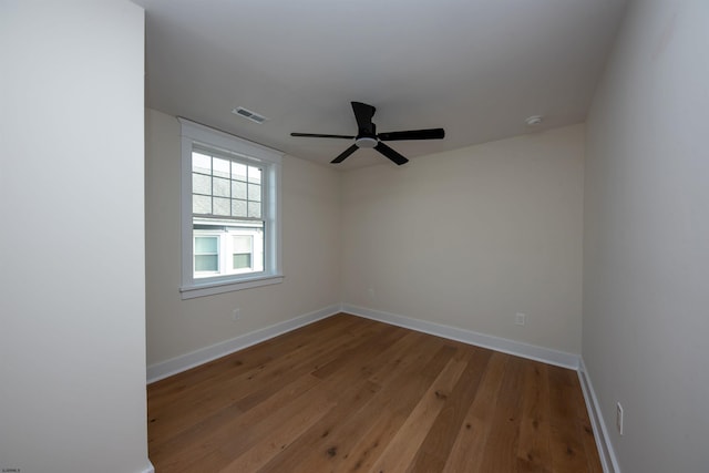 empty room featuring a ceiling fan, wood finished floors, visible vents, and baseboards