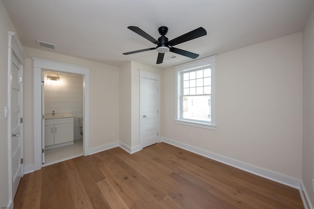 unfurnished bedroom with a sink, wood finished floors, visible vents, and baseboards