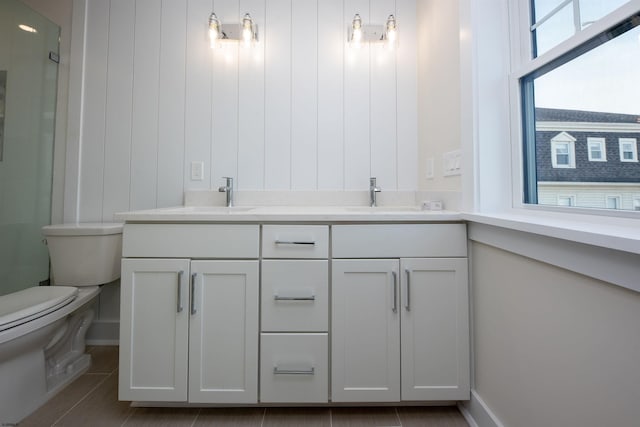 bathroom with toilet, a shower with door, double vanity, and a sink