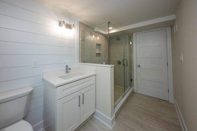 bathroom featuring toilet, wood finished floors, vanity, baseboards, and a stall shower