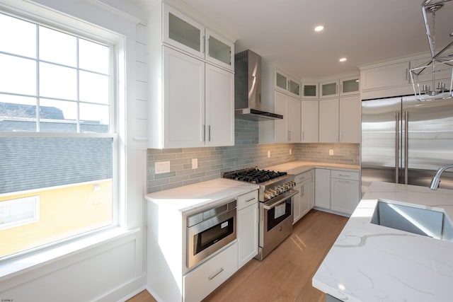 kitchen featuring a sink, wall chimney range hood, light wood-type flooring, tasteful backsplash, and high end appliances