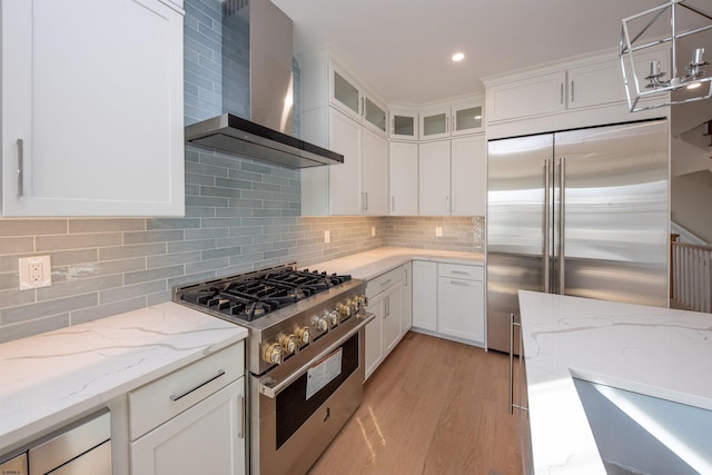 kitchen with high end appliances, white cabinetry, backsplash, and wall chimney exhaust hood