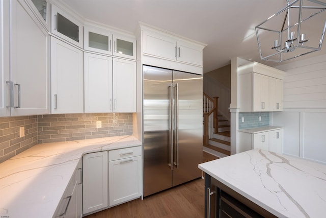 kitchen featuring built in fridge, light wood-style floors, white cabinets, backsplash, and glass insert cabinets