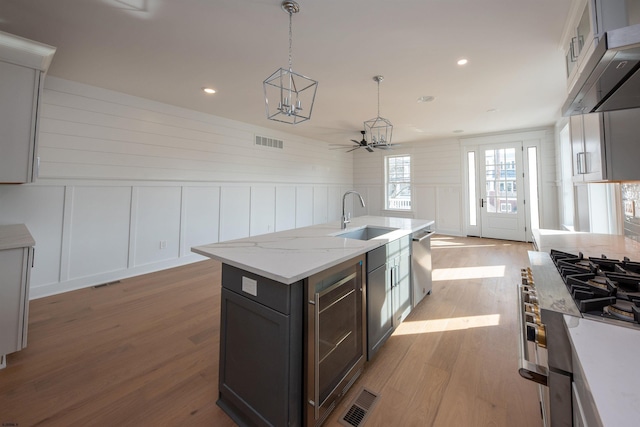 kitchen featuring a decorative wall, under cabinet range hood, wood finished floors, a sink, and stainless steel dishwasher