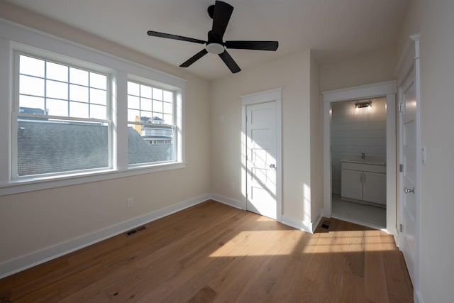 unfurnished bedroom with baseboards, visible vents, a ceiling fan, connected bathroom, and wood finished floors