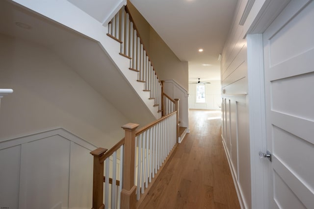 hall featuring recessed lighting, a decorative wall, light wood-style flooring, and stairs