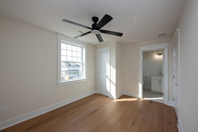 unfurnished bedroom with connected bathroom, wood finished floors, visible vents, and baseboards