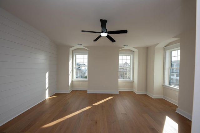 empty room with wood walls, baseboards, visible vents, and wood finished floors