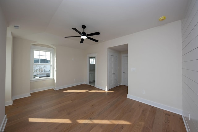 empty room featuring a ceiling fan, visible vents, baseboards, and wood finished floors