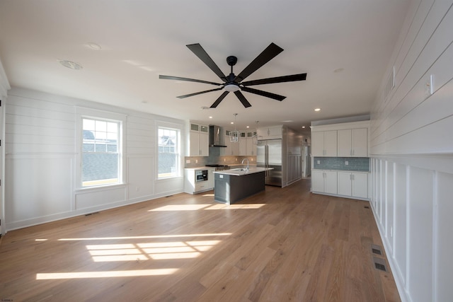 kitchen with wall chimney range hood, light wood-style flooring, backsplash, and built in fridge