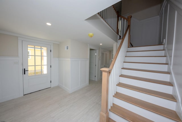 entryway with a decorative wall, a wainscoted wall, recessed lighting, stairway, and light wood finished floors