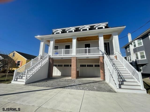 coastal inspired home with an attached garage, stairs, decorative driveway, and brick siding