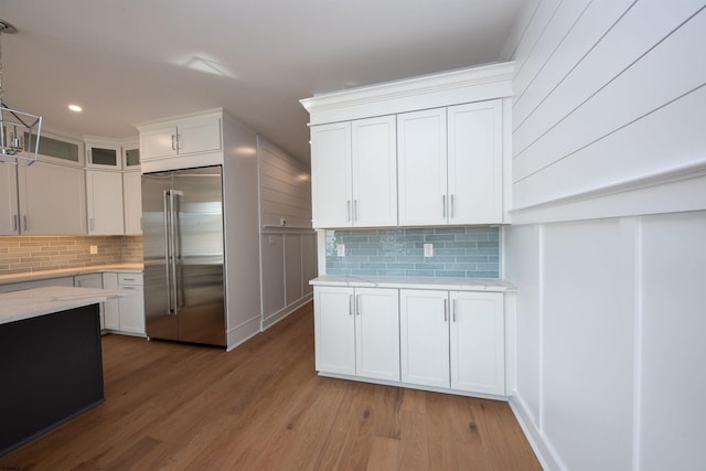 kitchen featuring light wood-type flooring, white cabinets, backsplash, and built in fridge