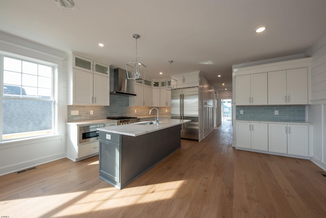 kitchen with visible vents, appliances with stainless steel finishes, light countertops, wall chimney range hood, and a sink