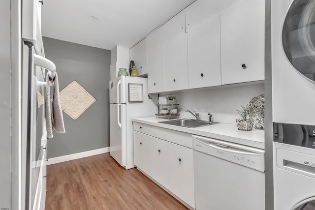 kitchen featuring white appliances, stacked washer / dryer, light wood-style flooring, light countertops, and a sink