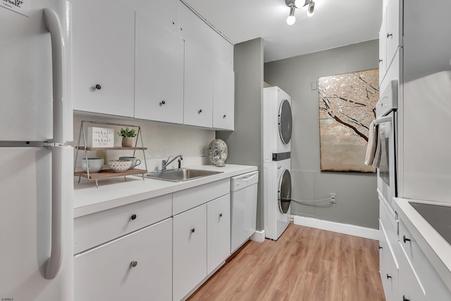 laundry room featuring laundry area, baseboards, stacked washer / dryer, light wood-style floors, and a sink