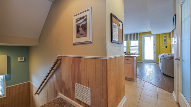 hall featuring light tile patterned floors, wooden walls, a wainscoted wall, an upstairs landing, and visible vents