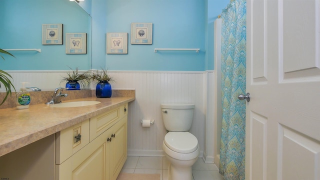 bathroom with a wainscoted wall, toilet, vanity, and tile patterned floors