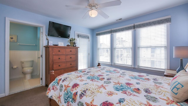 carpeted bedroom with a ceiling fan, wainscoting, visible vents, and ensuite bath