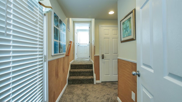 corridor with wood walls, stairs, dark colored carpet, and a wainscoted wall