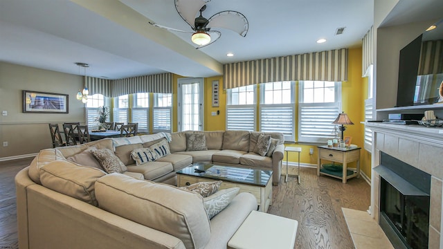 living room featuring a tile fireplace, wood finished floors, visible vents, baseboards, and a ceiling fan