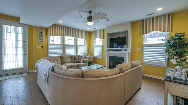 living room featuring ceiling fan, a fireplace, wood finished floors, visible vents, and baseboards