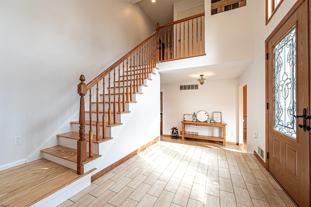 entrance foyer featuring visible vents, wood finished floors, a towering ceiling, and baseboards