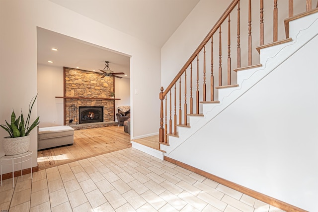 entryway with stairs, a stone fireplace, wood finished floors, and a ceiling fan