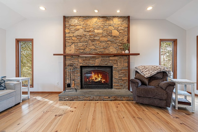 living room with lofted ceiling, a stone fireplace, baseboards, and hardwood / wood-style flooring