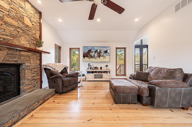 living room featuring lofted ceiling, a stone fireplace, light wood-type flooring, and visible vents