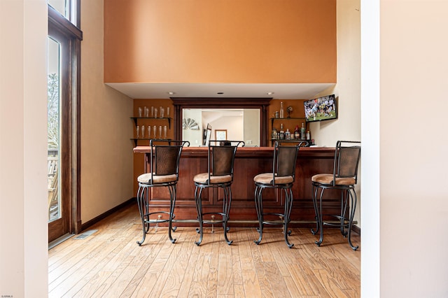 bar featuring baseboards, wood finished floors, a towering ceiling, and wet bar