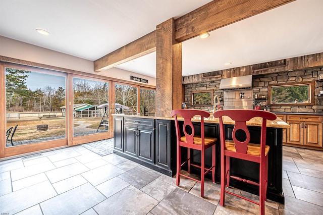 kitchen featuring visible vents, exhaust hood, light stone counters, beam ceiling, and recessed lighting