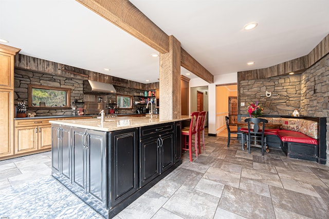 kitchen featuring light stone counters, recessed lighting, a kitchen breakfast bar, range hood, and stone finish floor