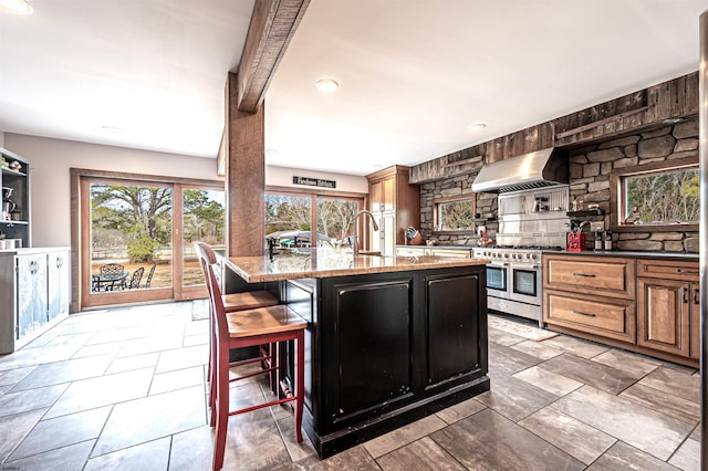 kitchen featuring a kitchen breakfast bar, double oven range, ventilation hood, light stone countertops, and tasteful backsplash