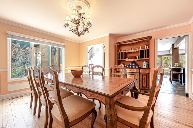 dining area featuring light wood finished floors, crown molding, baseboards, and a notable chandelier